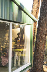 Älterer Mann steht am Fenster eines Hauses und schaut hinaus - JCCMF08515