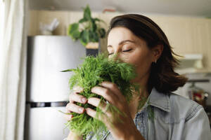 Mature woman smelling dill leaves at home - TYF00495