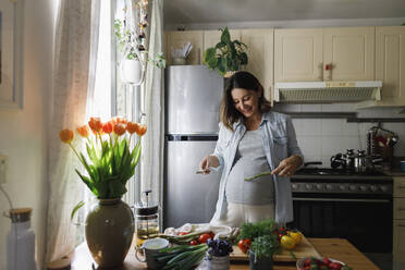 Happy woman with asparagus sticks standing in kitchen at home - TYF00496