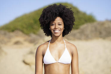 Happy woman with Afro hairstyle in bikini standing at beach - JSMF02558