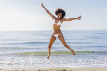 Cheerful young woman jumping in front of sea on sunny day - JSMF02562