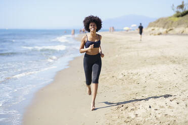 Glückliche junge Frau, die am Strand läuft - JSMF02593