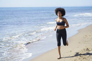 Junge Frau läuft am Strand an einem sonnigen Tag - JSMF02594