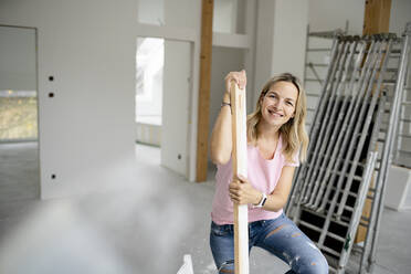 Happy woman holding wooden plank in apartment - HMEF01490
