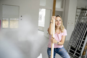 Smiling woman leaning on plank in apartment - HMEF01491