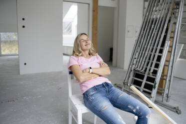 Lächelnde Frau mit geschlossenen Augen in einer Wohnung sitzend - HMEF01496