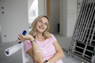 Contemplative woman with paint roller sitting on chair - HMEF01500