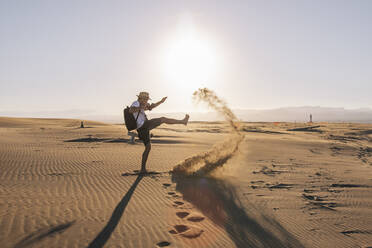 Playful man kicking sand on beach at sunset - MMPF00538
