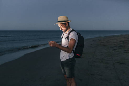 Smiling man using smart phone on beach at night - MMPF00543