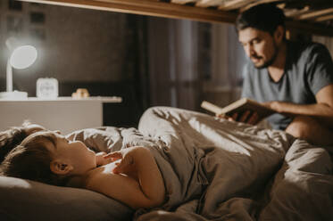 Father reading book to children on bed - ANAF00621