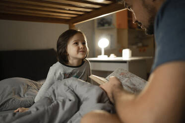 Smiling son looking at father reading book at home - ANAF00623