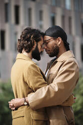 Homosexuelles Paar mit geschlossenen Augen, das sich vor einem Gebäude umarmt - AGOF00314