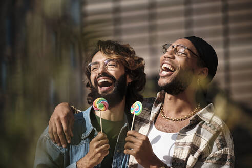 Happy gay couple eating lollipops on sunny day - AGOF00317