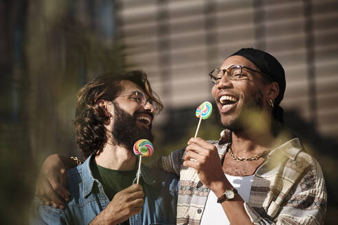 Happy gay couple eating rainbow candy - AGOF00318