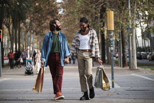 Gay couple holding hands walking on street - AGOF00319