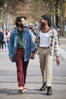 Smiling gay couple holding hands walking on road - AGOF00320