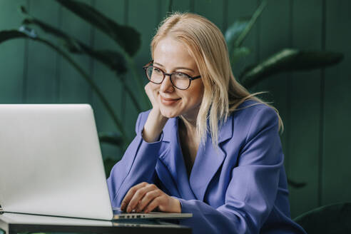 Smiling businesswoman using laptop at home office - VSNF00156