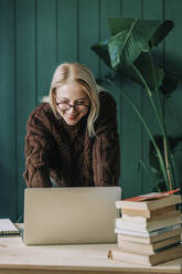 Smiling businesswoman working on laptop leaning at desk in home office - VSNF00163