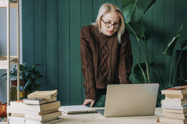 Businesswoman wearing sweater watching laptop at home office - VSNF00164