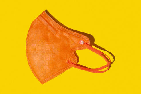 Orange colored FFP2 mask lying against yellow background - GIOF15711