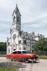 Cuba, Havana, Red vintage car parked in front of white painted church in La Vibora neighborhood - MMPF00550