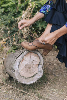 Frau bindet Schnürsenkel und hält Bein auf Baumstumpf - MMPF00565