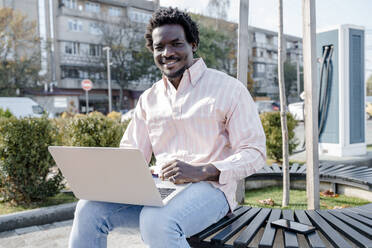 Lächelnder Freiberufler mit Laptop auf einer Bank sitzend - OSF01157