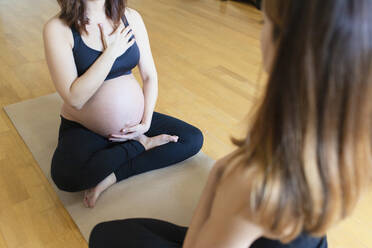 Schwangere Frau, die ihre Hand auf Bauch und Brust hält, übt Yoga mit einem Lehrer im Studio - MMPF00568