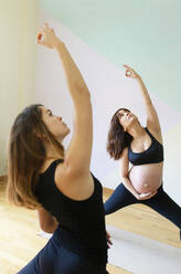 Yogalehrer mit erhobener Hand unterrichtet eine schwangere Frau im Studio - MMPF00571