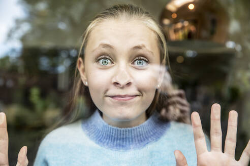 Smiling girl pressing nose on glass window - PMF02330