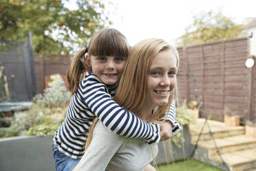 Smiling girl giving piggyback ride to sister in garden - PMF02334