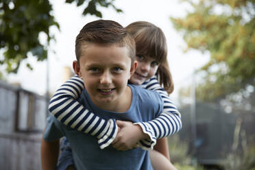 Playful boy giving piggyback ride to sister in garden - PMF02341