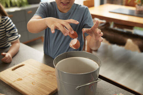 Hand eines Jungen, der zu Hause eine Eierschale in den Mülleimer wirft - PMF02366