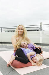 Lächelnde Frau mit Töchtern auf Übungsmatte auf dem Dach - AANF00400