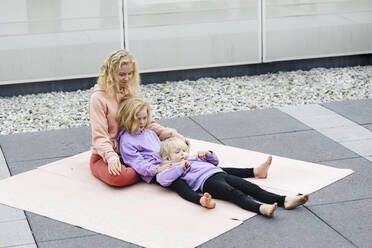 Girls lying on exercise mat with mother at rooftop - AANF00410