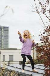 Girl holding stick dancing on rooftop in front of sky - AANF00414