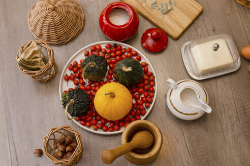 Pumpkins, rose hips, chestnuts, sugar bowl, mortal and pestle, milk jug and butter lying on wooden surface - LLUF01038