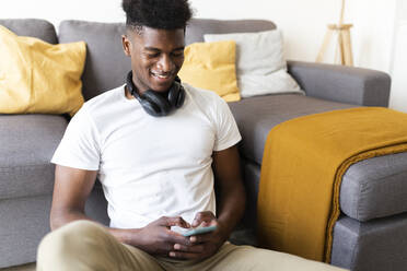 Lächelnder Mann, der ein Mobiltelefon benutzt und zu Hause auf dem Sofa sitzt - JPTF01136