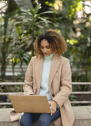 Young businesswoman using laptop on bench - JCCMF08525