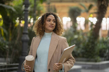 Young businesswoman holding laptop and disposable cup - JCCMF08529