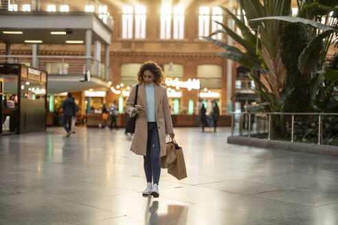 Junge Frau mit Einkaufstüten und Mobiltelefon am Bahnhof - JCCMF08541