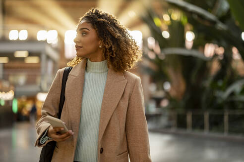 Young woman holding mobile phone at station - JCCMF08543