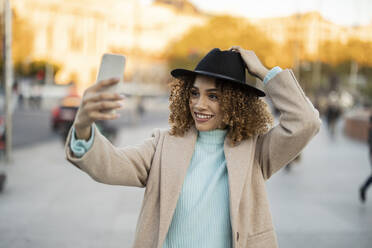 Lächelnde Frau mit Hut, die ein Selfie mit ihrem Mobiltelefon macht - JCCMF08576