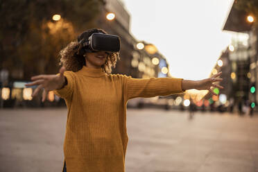 Woman wearing virtual reality simulator gesturing on footpath - JCCMF08598