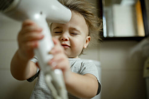 Boy with eyes closed blowing hair with dryer at home - ANAF00630