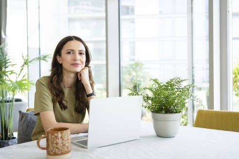 Smiling businesswoman sitting with laptop at home - SVKF00826