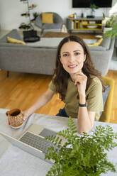 Geschäftsfrau sitzend Hand auf Kinn durch Laptop auf Tisch zu Hause - SVKF00830