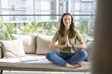 Smiling woman with eyes closed meditating on sofa at home - SVKF00854