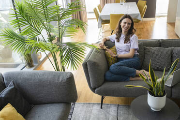 Happy woman with diary sitting on sofa at home - SVKF00863