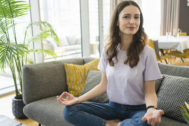 Smiling woman meditating on sofa in living room - SVKF00874